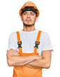 © Krakenimages.com - Hispanic young man wearing handyman uniform and safety hardhat skeptic and nervous, disapproving expression on face with crossed arms. negative person.