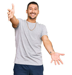 Wall Mural - Handsome man with tattoos wearing 90s style looking at the camera smiling with open arms for hug. cheerful expression embracing happiness.