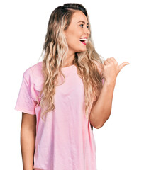 Poster - Young blonde woman wearing casual pink t shirt pointing thumb up to the side smiling happy with open mouth