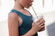 © ADDICTIVE STOCK - Side view of cropped unrecognizable adorable boy dressed in blue tank top drinking cold coffee with straw while standing on footpath during summer vacation