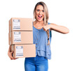 © Krakenimages.com - Young beautiful blonde woman holding delivery boxes smiling happy pointing with hand and finger