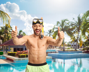 Wall Mural - Man in a swimsuit with a diving mask showing thumbs up in front of a swimming pool