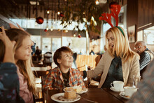 Festive Mother Wearing Reindeer Antlers Sitting In Cafe With Kids
