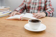 © O.Farion - Cup of coffee on wooden table, unrecognizable man reading book, studying or working, sitting at the desk with stack of books, focus on foreground