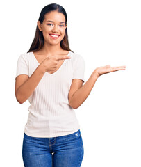 Sticker - Young beautiful latin girl wearing casual white t shirt amazed and smiling to the camera while presenting with hand and pointing with finger.