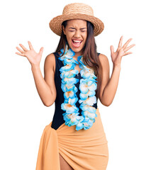 Sticker - Young beautiful latin girl wearing hawaiian lei and summer hat celebrating mad and crazy for success with arms raised and closed eyes screaming excited. winner concept