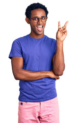 Wall Mural - African handsome man wearing casual clothes and glasses smiling with happy face winking at the camera doing victory sign. number two.