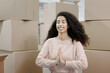 © MyJuly - moving to new apartment relocation. happy young woman sits in lotus position and meditates among packed boxes of personal belongings, an African American lady relaxes and waits for transfer service