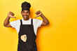 African American cook with utensils, yellow studio, feels proud and self confident, example to follow.