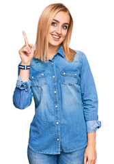 Wall Mural - Beautiful caucasian woman wearing casual denim jacket showing and pointing up with finger number one while smiling confident and happy.