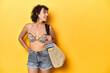 Summer ready woman with beach gear and plane ticket, yellow studio backdrop.