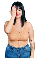 Sticker - Young hispanic plus size woman wearing casual clothes covering one eye with hand, confident smile on face and surprise emotion.