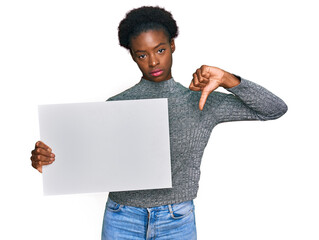 Sticker - Young african american girl holding blank empty banner with angry face, negative sign showing dislike with thumbs down, rejection concept