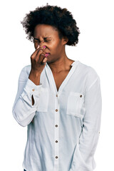 Sticker - African american woman with afro hair wearing casual white t shirt smelling something stinky and disgusting, intolerable smell, holding breath with fingers on nose. bad smell