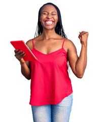 Wall Mural - Young african american woman holding touchpad screaming proud, celebrating victory and success very excited with raised arms