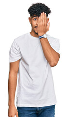 Wall Mural - Young arab man wearing casual white t shirt covering one eye with hand, confident smile on face and surprise emotion.