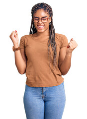 Poster - Young african american woman with braids wearing casual clothes and glasses very happy and excited doing winner gesture with arms raised, smiling and screaming for success. celebration concept.