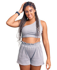 Wall Mural - Young african american woman with braids wearing sportswear confuse and wonder about question. uncertain with doubt, thinking with hand on head. pensive concept.