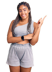 Sticker - Young african american woman with braids wearing sportswear with a big smile on face, pointing with hand and finger to the side looking at the camera.