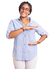 Poster - Young african american woman with braids wearing casual clothes and glasses gesturing with hands showing big and large size sign, measure symbol. smiling looking at the camera. measuring concept.