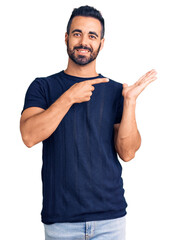 Canvas Print - Young hispanic man wearing casual clothes amazed and smiling to the camera while presenting with hand and pointing with finger.