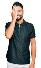 Poster - Young man with beard wearing sportswear covering one eye with hand, confident smile on face and surprise emotion.