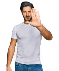 Young hispanic man wearing casual white t shirt doing stop sing with palm of the hand. warning expression with negative and serious gesture on the face.