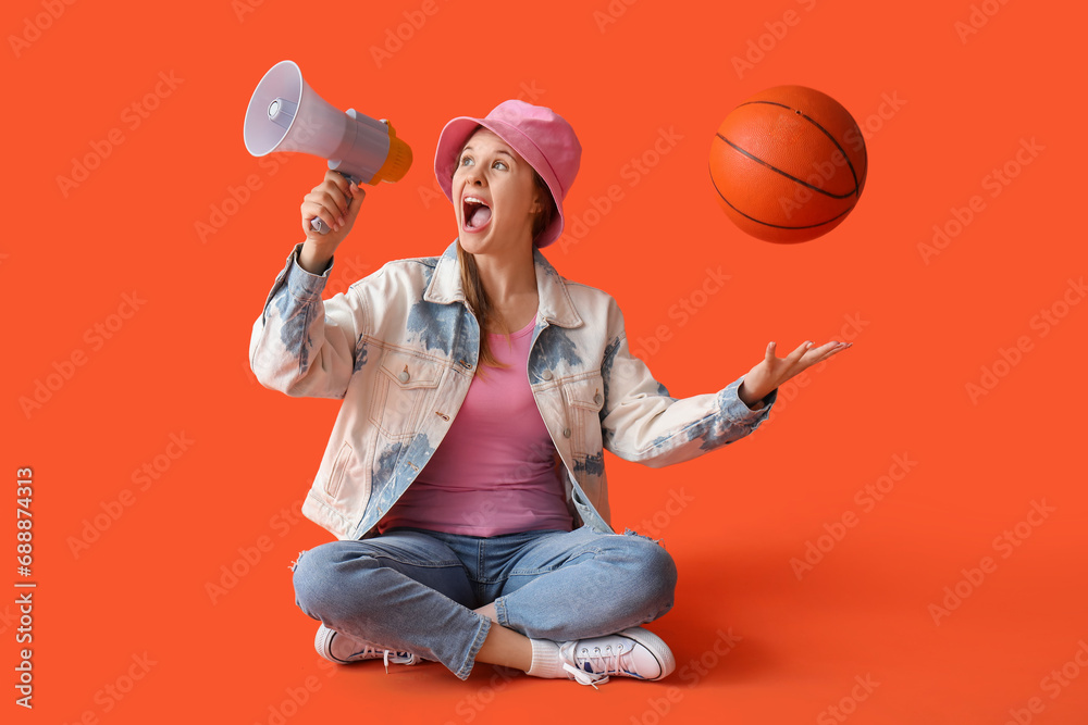 Young woman with ball shouting into megaphone on red background