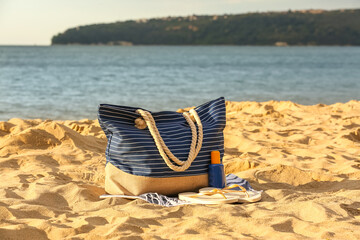 Summer bag with different beach accessories on sand near ocean at resort