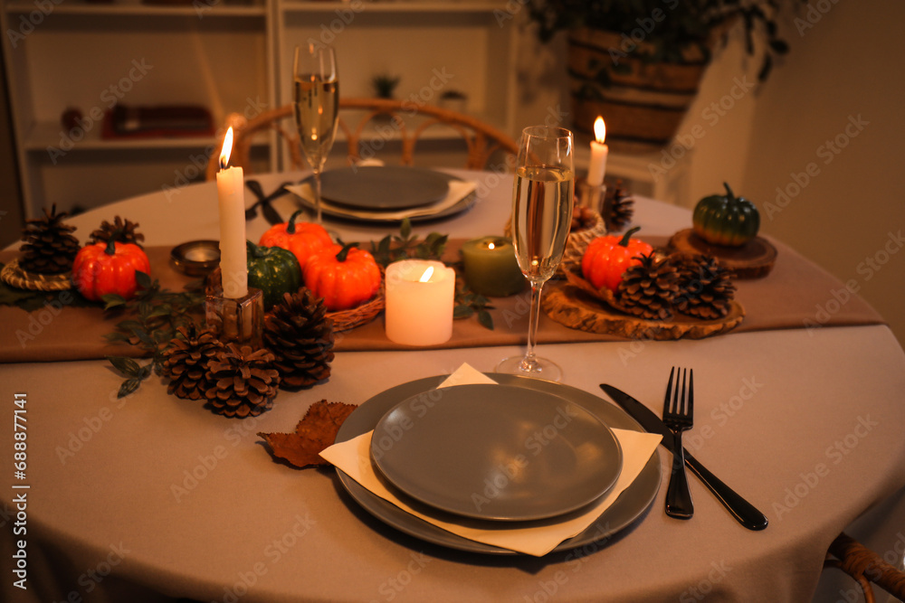 Autumn table setting with pumpkins, burning candles and pine cones at evening