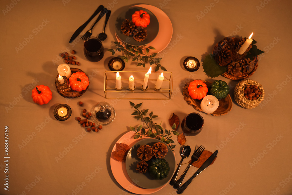 Autumn table setting with pumpkins, burning candles and pine cones at evening