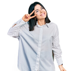 Poster - Young brunette woman with blue eyes wearing oversize white shirt doing peace symbol with fingers over face, smiling cheerful showing victory