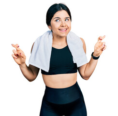 Poster - Young brunette woman with blue eyes wearing sportswear and towel gesturing finger crossed smiling with hope and eyes closed. luck and superstitious concept.