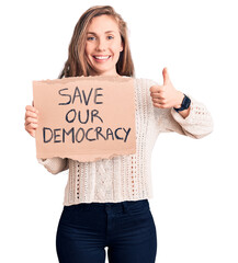 Sticker - Young beautiful blonde woman holding save our democracy banner smiling happy and positive, thumb up doing excellent and approval sign