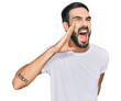 Young hispanic man wearing casual white t shirt shouting and screaming loud to side with hand on mouth. communication concept.