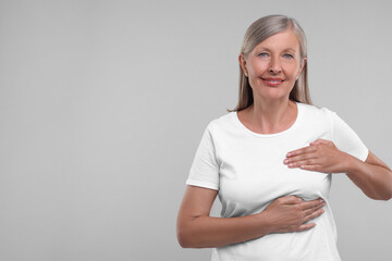 Poster - Beautiful senior woman doing breast self-examination on light grey background, space for text