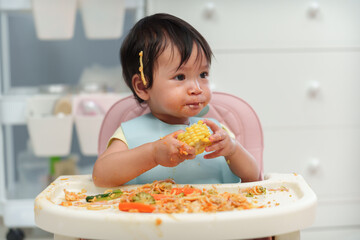 infant baby eating food and vegetable by self feeding BLW or baby led weaning on chair