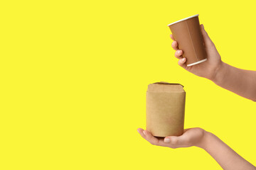 Wall Mural - Female hands with takeaway paper cup and box on yellow background