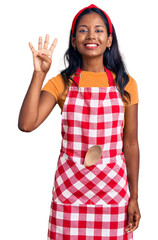 Wall Mural - Young indian girl wearing professional baker apron showing and pointing up with fingers number four while smiling confident and happy.