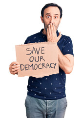 Wall Mural - Middle age handsome man holding save our democracy cardboard banner covering mouth with hand, shocked and afraid for mistake. surprised expression