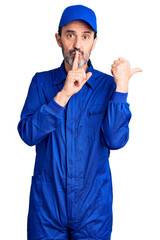 Poster - Middle age handsome man wearing mechanic uniform asking to be quiet with finger on lips pointing with hand to the side. silence and secret concept.