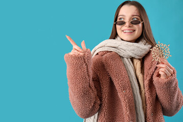 Sticker - Young woman in winter clothes with snowflake pointing at something on blue background