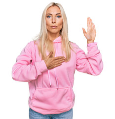 Poster - Young blonde woman wearing casual sweatshirt swearing with hand on chest and open palm, making a loyalty promise oath