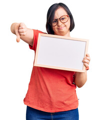 Sticker - Brunette woman with down syndrome holding empty white chalkboard with angry face, negative sign showing dislike with thumbs down, rejection concept