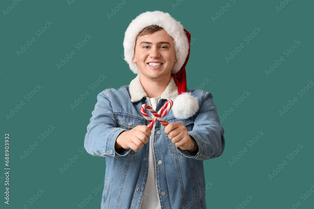 Happy young man in Santa hat with candy canes on green background
