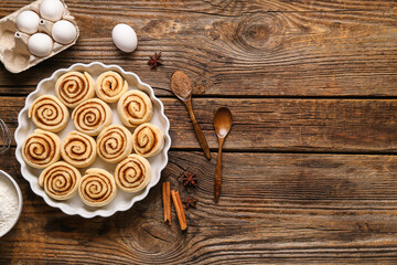 Wall Mural - Baking dish with uncooked cinnamon rolls and ingredients on wooden background