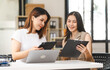 © NanSan - Two Asian colleagues, freelance writer and graphic designer discussing about creating characters in screenplays work and smiling with tablets and a laptop, journalist, artist, meeting together