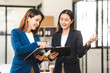 © NanSan - Two middle aged and young Asian female executives in formal suits review bar chart, discussing business strategies in office setting, senior executives or directors in advertising or public relations