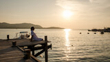 Fototapeta Sypialnia - Asian woman watching sunset at a wooden pier in the ocean during sunset in Samaesan Thailand