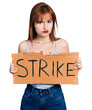 © Krakenimages.com - Redhead young woman holding strike banner cardboard skeptic and nervous, frowning upset because of problem. negative person.